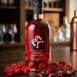 Framboise-boutons-de-rose-la-bouteille-de-ce-divin-punch-au-rhum-a-une-superbe-robe-rose-gourmande-elle-est-posée-sur-une-table-en-bois-et-est-entourée-de-belles-framboises-fraiches